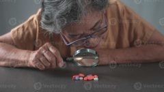 old-woman-looking-through-a-magnifying-glass-at-colorful-pills-on-the-table-photo