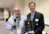 Michael Fuljenz Wins NLG Award for Metals Market Report Dr. Michael Fuljenz stands at left holding an award plaque and addressing seated guests while Scott A. Travers, at right, presents the plaque at the Numismatic Literary Guild awards luncheon.