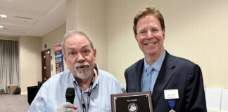 Michael Fuljenz Wins NLG Award for Metals Market Report Dr. Michael Fuljenz stands at left holding an award plaque and addressing seated guests while Scott A. Travers, at right, presents the plaque at the Numismatic Literary Guild awards luncheon.